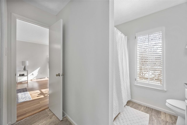 bathroom featuring a shower with curtain, wood finished floors, toilet, and baseboards