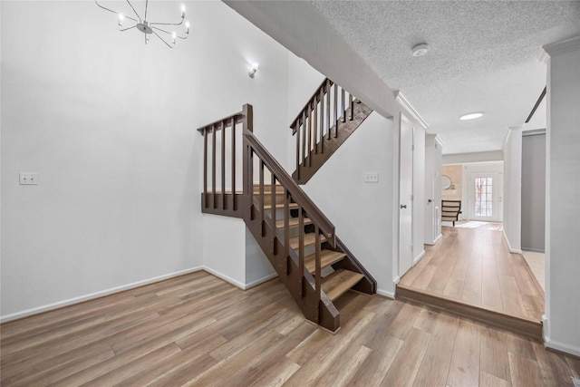 stairway featuring a notable chandelier, a textured ceiling, baseboards, and wood finished floors