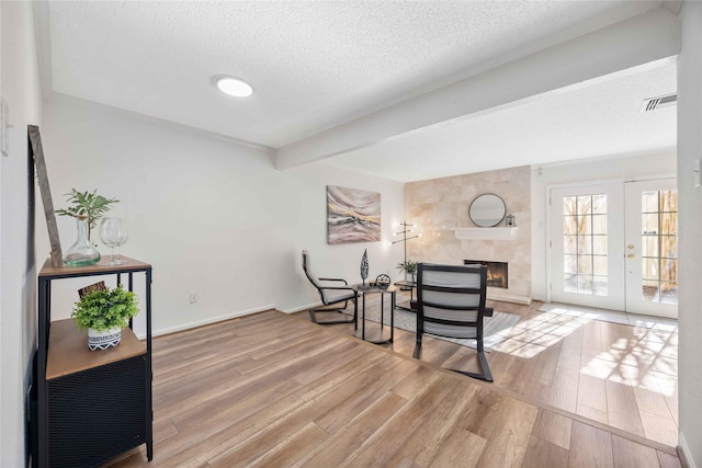 sitting room with a textured ceiling, wood finished floors, visible vents, beamed ceiling, and a tiled fireplace