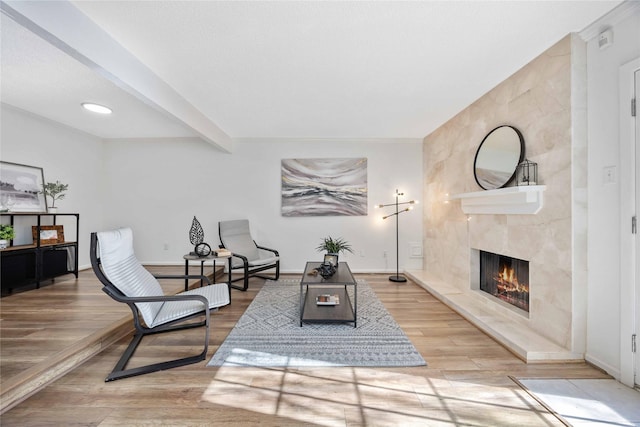 sitting room with beam ceiling, a fireplace, light wood-style flooring, and baseboards