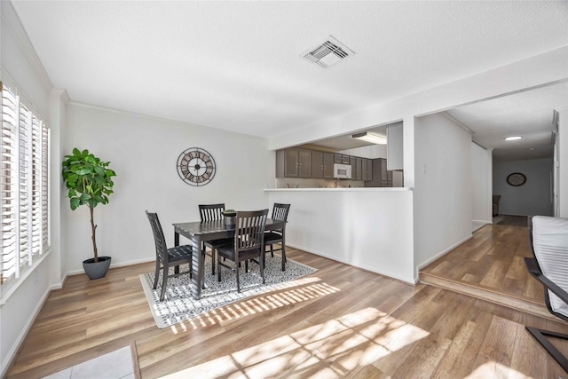 dining room with a textured ceiling, light wood finished floors, visible vents, and baseboards