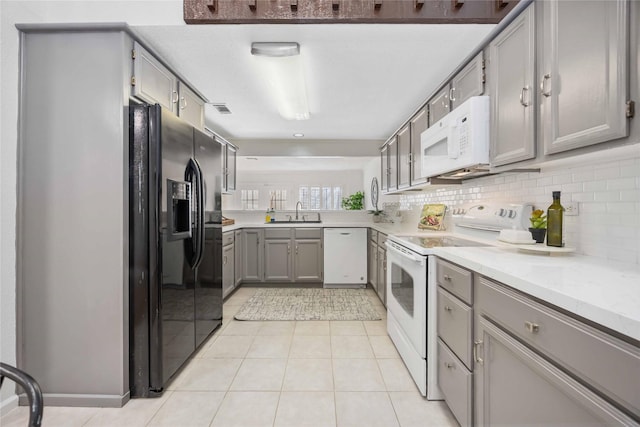 kitchen with tasteful backsplash, white appliances, a sink, and gray cabinetry