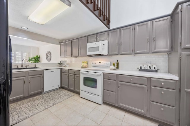 kitchen featuring white appliances, tasteful backsplash, gray cabinets, light countertops, and a sink