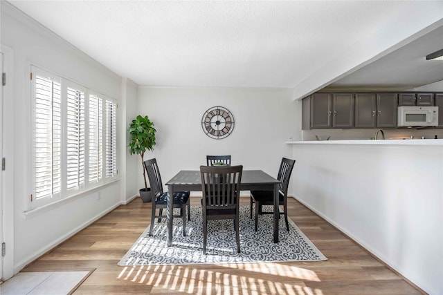 dining area with light wood-type flooring, a textured ceiling, and baseboards