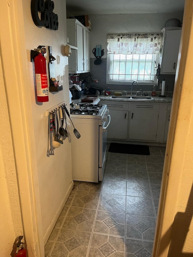 kitchen with decorative backsplash, tile patterned floors, a sink, and white range with gas cooktop