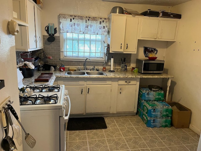 kitchen featuring white range with gas stovetop, stainless steel microwave, backsplash, and a sink