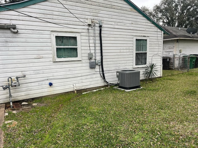 view of side of home featuring central AC, a lawn, and fence