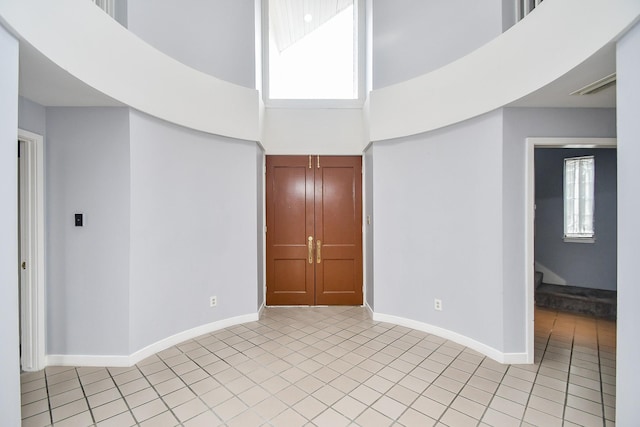 unfurnished room featuring a towering ceiling, light tile patterned floors, visible vents, and baseboards