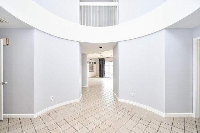 corridor with light tile patterned floors, a high ceiling, visible vents, and baseboards