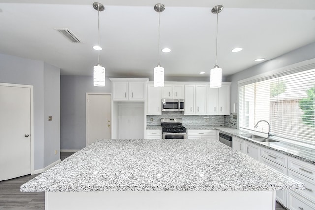 kitchen with visible vents, a kitchen island, appliances with stainless steel finishes, white cabinetry, and a sink