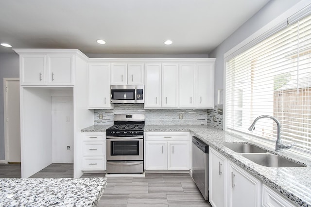 kitchen with light stone counters, stainless steel appliances, a sink, white cabinets, and tasteful backsplash