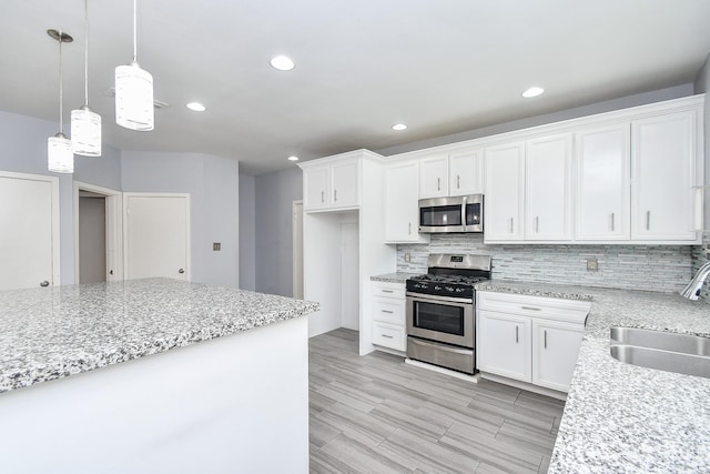 kitchen featuring stainless steel appliances, tasteful backsplash, hanging light fixtures, white cabinetry, and a sink