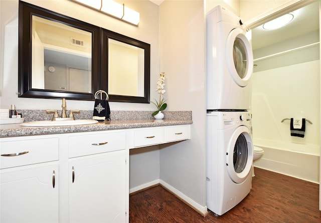 laundry room with dark wood-type flooring, visible vents, a sink, and stacked washing maching and dryer