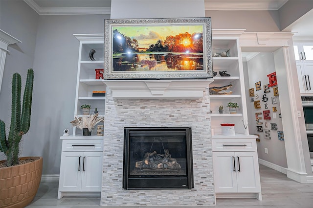 living area with baseboards, built in features, a glass covered fireplace, ornamental molding, and light wood-style floors