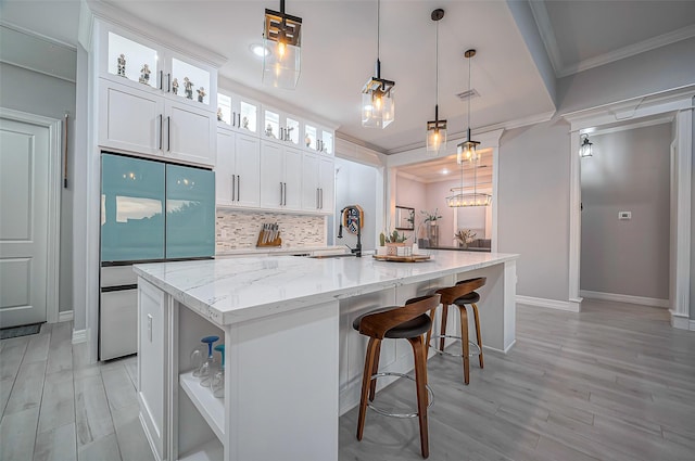 kitchen featuring decorative backsplash, a large island, light stone countertops, crown molding, and built in fridge