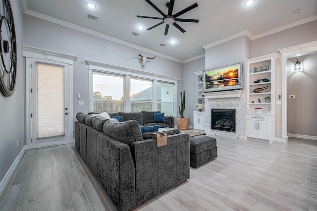 living area featuring crown molding, visible vents, light wood-style floors, a glass covered fireplace, and baseboards