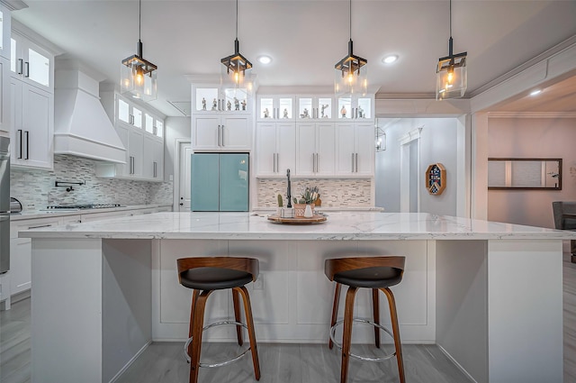 kitchen with premium range hood, a spacious island, white cabinets, fridge, and stainless steel gas stovetop