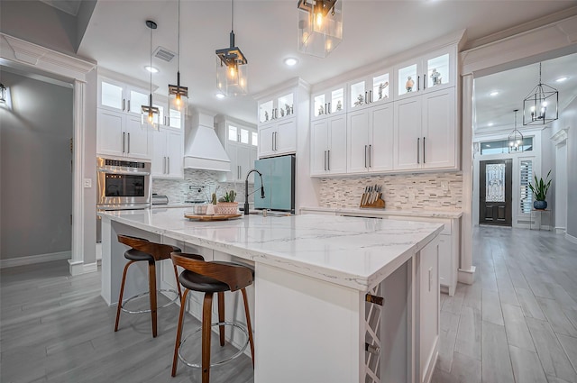 kitchen featuring premium range hood, a sink, visible vents, white cabinets, and high end fridge