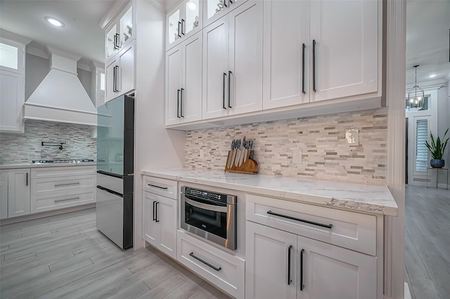 kitchen with light stone counters, premium range hood, white cabinetry, appliances with stainless steel finishes, and light wood finished floors