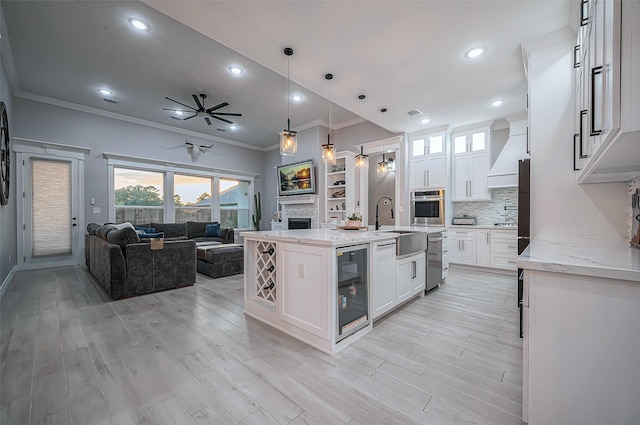 kitchen featuring oven, a fireplace, white cabinets, open floor plan, and a center island with sink