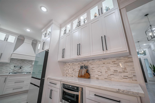 kitchen with appliances with stainless steel finishes, custom range hood, light stone counters, and white cabinetry