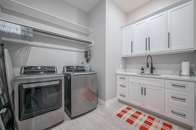 clothes washing area with light wood finished floors, cabinet space, washing machine and dryer, a sink, and baseboards