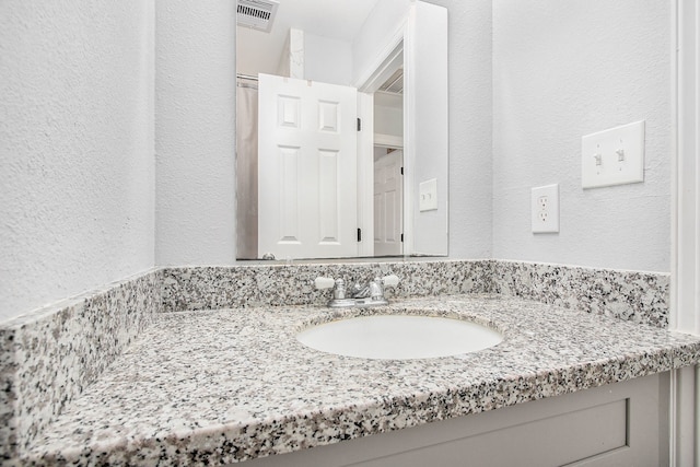 bathroom with visible vents, a textured wall, and vanity