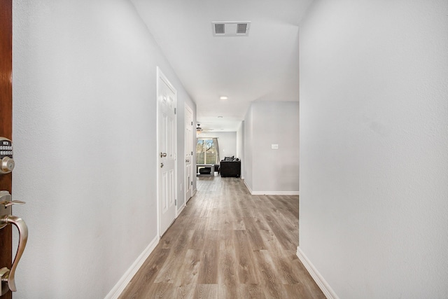 hallway with baseboards, visible vents, and light wood finished floors