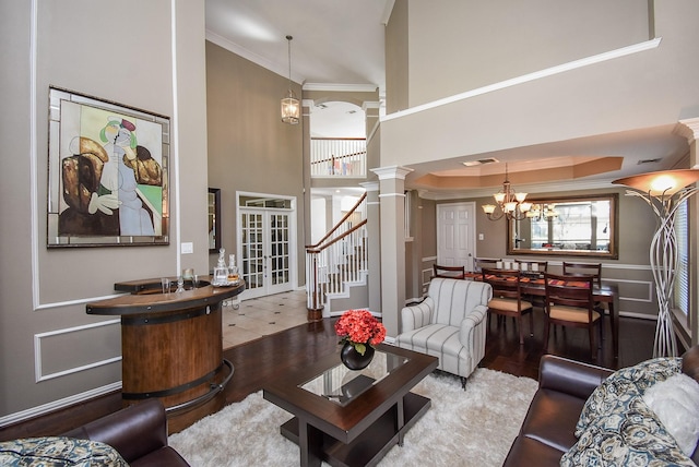 living area featuring a notable chandelier, crown molding, wood finished floors, ornate columns, and stairs