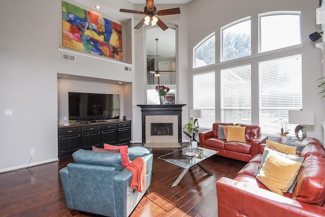 living room featuring dark wood-style floors, baseboards, a towering ceiling, and a tiled fireplace