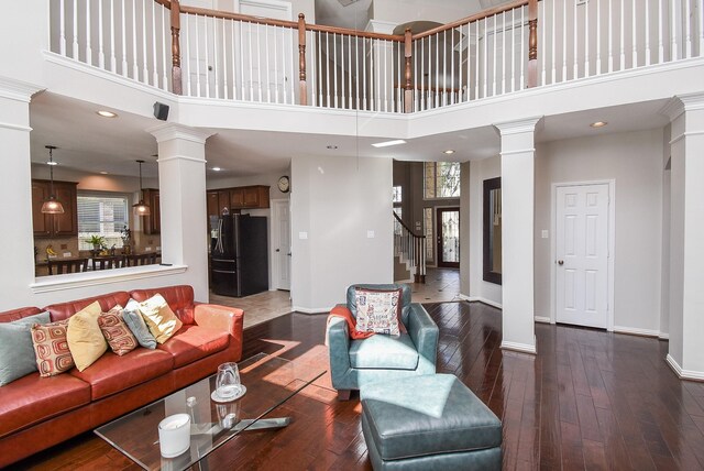 living room featuring stairway, dark wood finished floors, a towering ceiling, and ornate columns