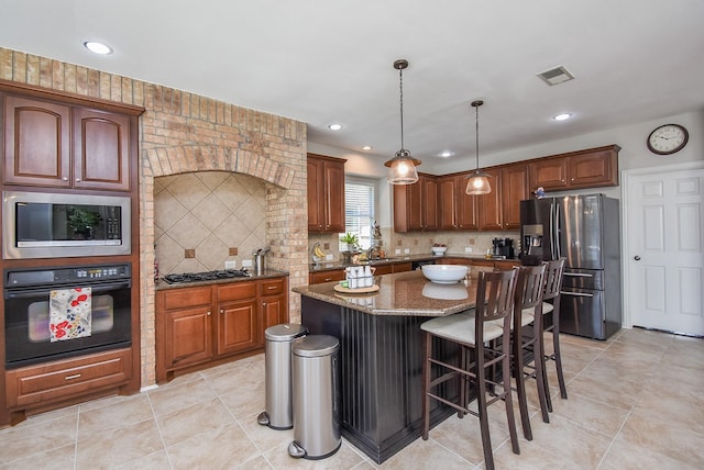 kitchen featuring decorative backsplash, dark stone countertops, a center island, stainless steel appliances, and a sink