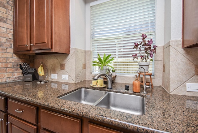 kitchen with brown cabinets, tasteful backsplash, dark stone countertops, and a sink
