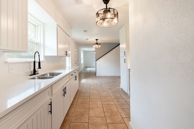 kitchen with pendant lighting, white cabinets, a sink, and an inviting chandelier