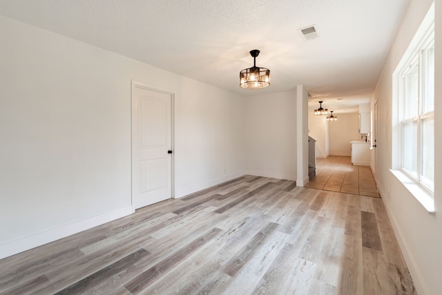 unfurnished room featuring an inviting chandelier, baseboards, visible vents, and light wood-style floors