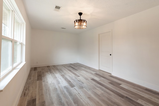 unfurnished room with visible vents, a textured ceiling, light wood-style flooring, and baseboards