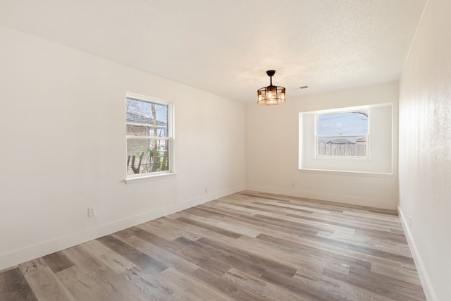 spare room with light wood-type flooring, a textured ceiling, and baseboards