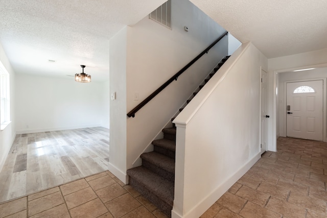 stairway featuring stone finish floor, visible vents, a textured ceiling, and baseboards