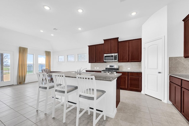 kitchen featuring a sink, a kitchen bar, decorative backsplash, stainless steel appliances, and a kitchen island with sink