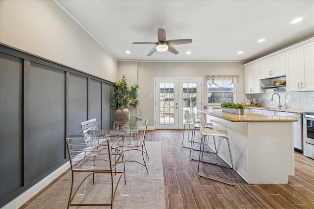 kitchen with light stone counters, wood finished floors, a center island, french doors, and backsplash