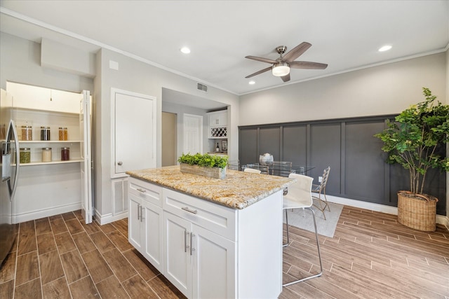 kitchen featuring wood finish floors, a kitchen island, white cabinetry, and light stone countertops