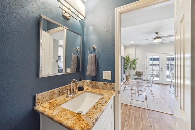 bathroom featuring wood finish floors, french doors, a textured wall, a ceiling fan, and vanity