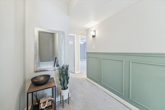 corridor featuring a wainscoted wall, carpet, and a decorative wall