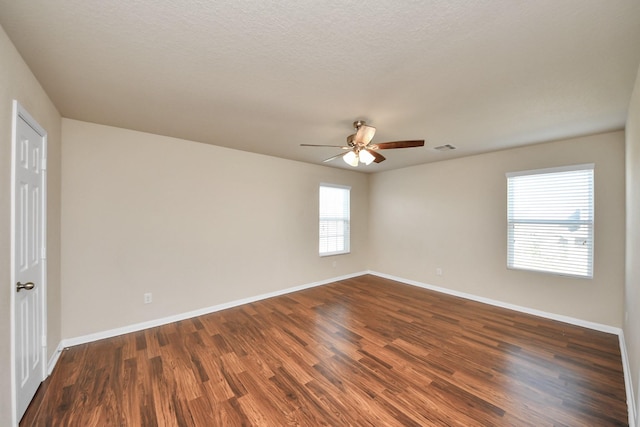 spare room with baseboards, visible vents, dark wood finished floors, and a ceiling fan