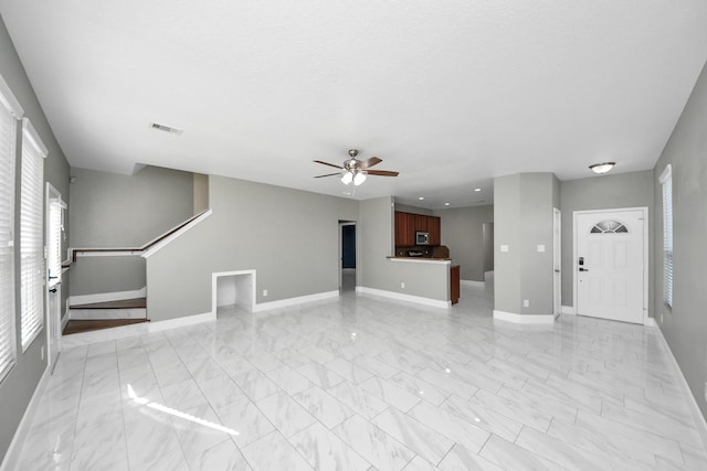 unfurnished living room featuring ceiling fan, visible vents, baseboards, marble finish floor, and stairway