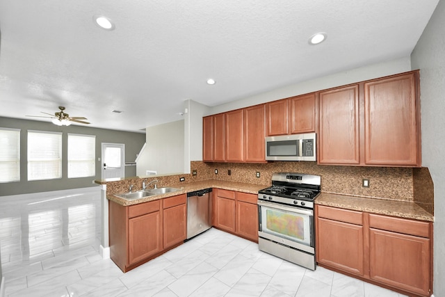 kitchen with a peninsula, a sink, appliances with stainless steel finishes, backsplash, and brown cabinetry