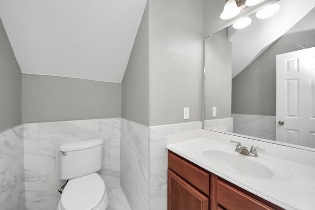 half bathroom featuring toilet, a wainscoted wall, vanity, tile walls, and vaulted ceiling