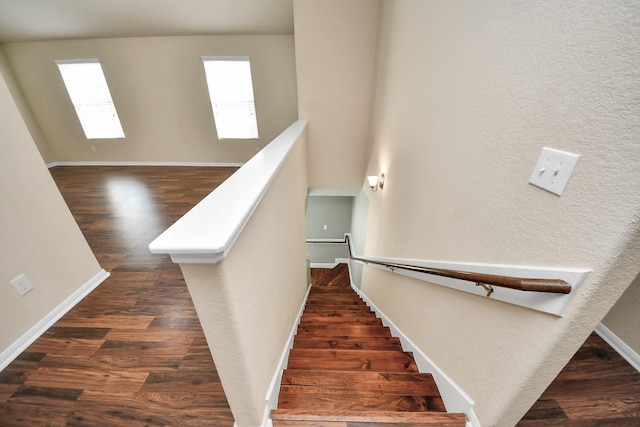 staircase featuring a textured wall, wood finished floors, and baseboards