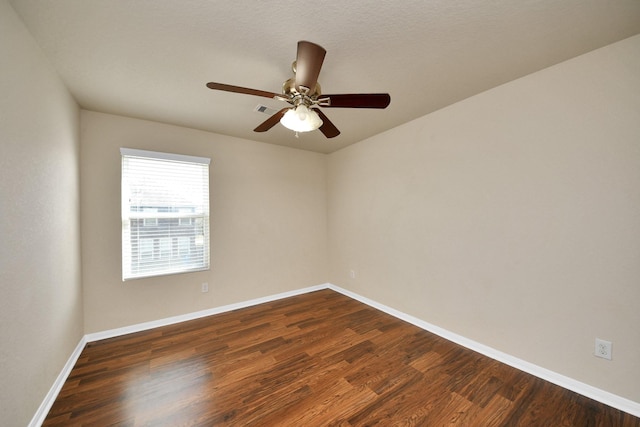 empty room featuring dark wood-style floors, ceiling fan, visible vents, and baseboards