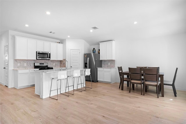 kitchen featuring a breakfast bar, light wood finished floors, stainless steel appliances, visible vents, and an island with sink